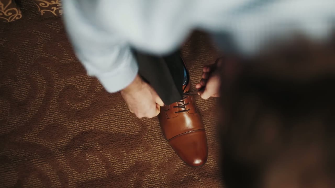 Close-up of brown leather dress shoes being tied on a patterned carpet