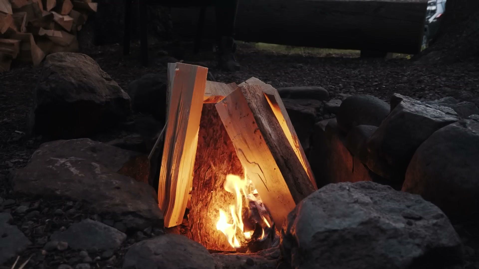 A campfire burning between rocks, with orange coals low down and brighter flames above them.