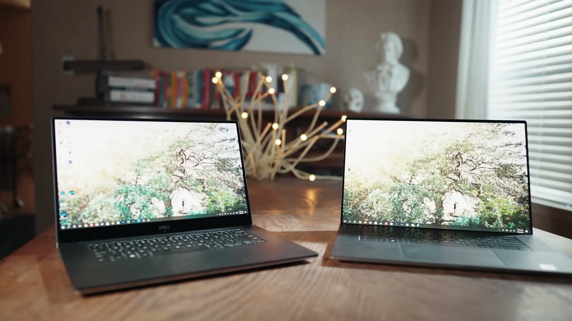 The Dell XPS 15 and the larger Dell XPS 17 open side by side on a wooden table, both showing the same desktop wallpaper