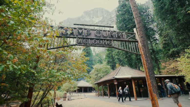 The rustic timber Camp Curry welcome arch in Yosemite Valley with granite walls rising behind the trees