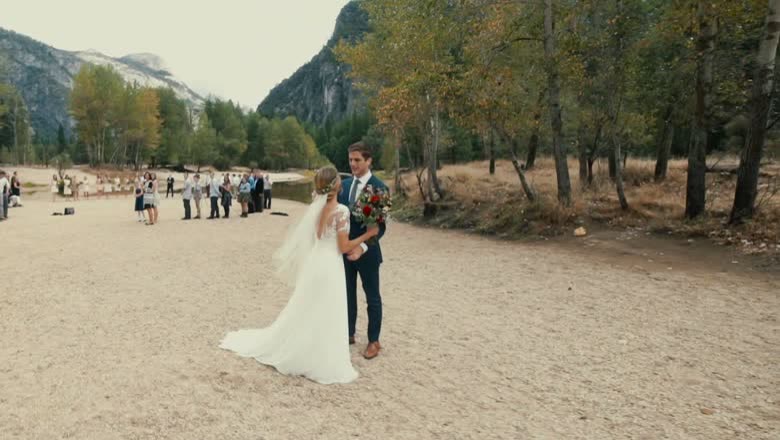 The couple standing together on Sentinel Beach in front of a small group of guests, with the valley walls and river behind
