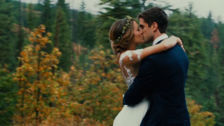 The bride and groom kissing in a clearing with autumn-coloured forest sweeping past behind them