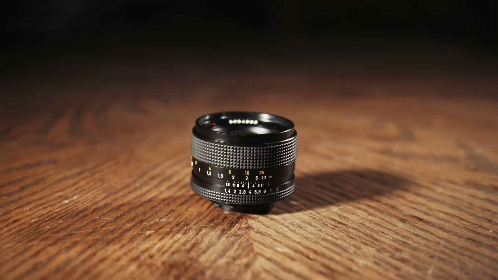 A small Zeiss Contax 50mm manual lens sitting on a wooden table