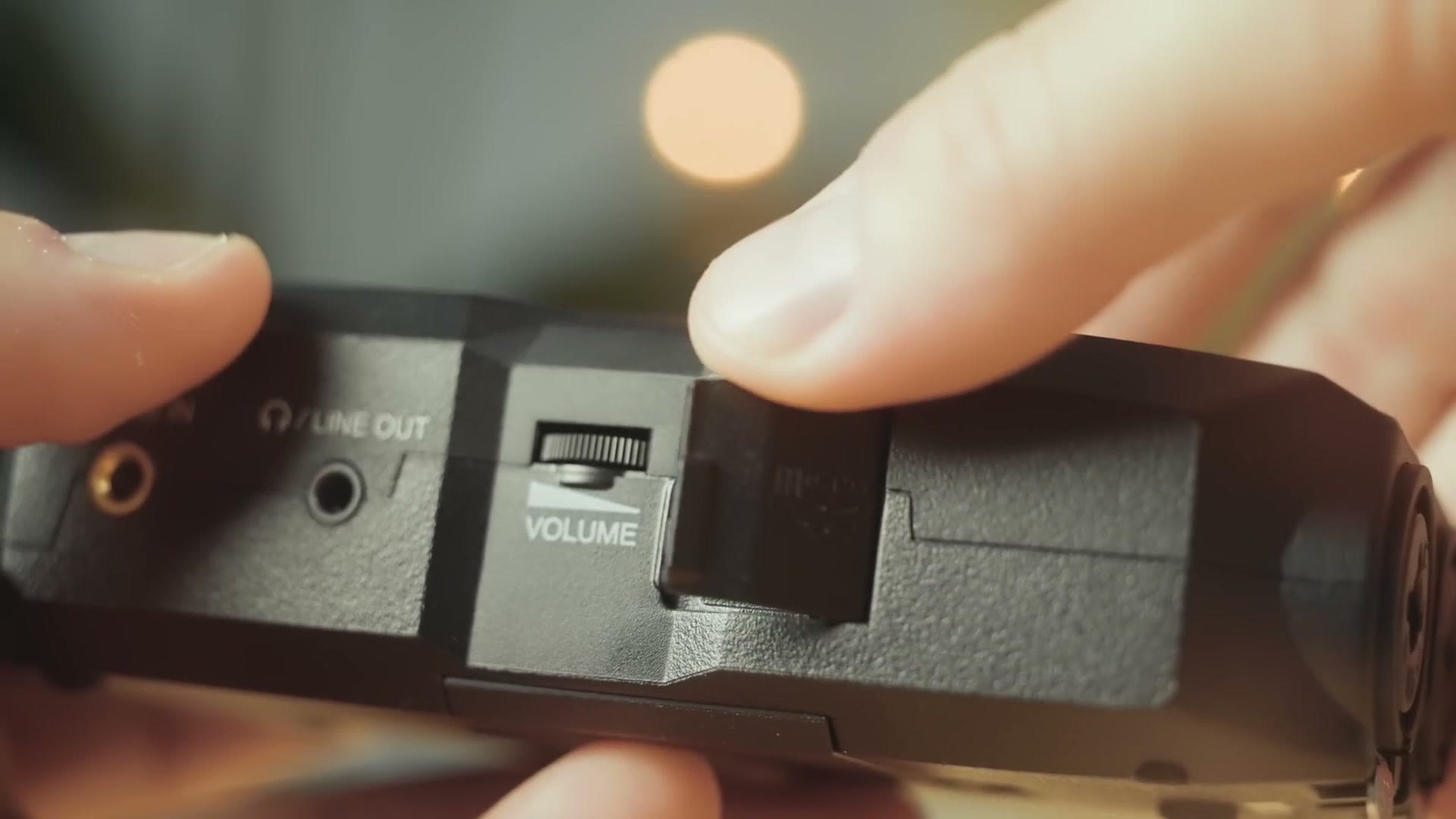 Side panel of the Zoom H4essential showing the line out jack, volume slider and the SD card door being opened