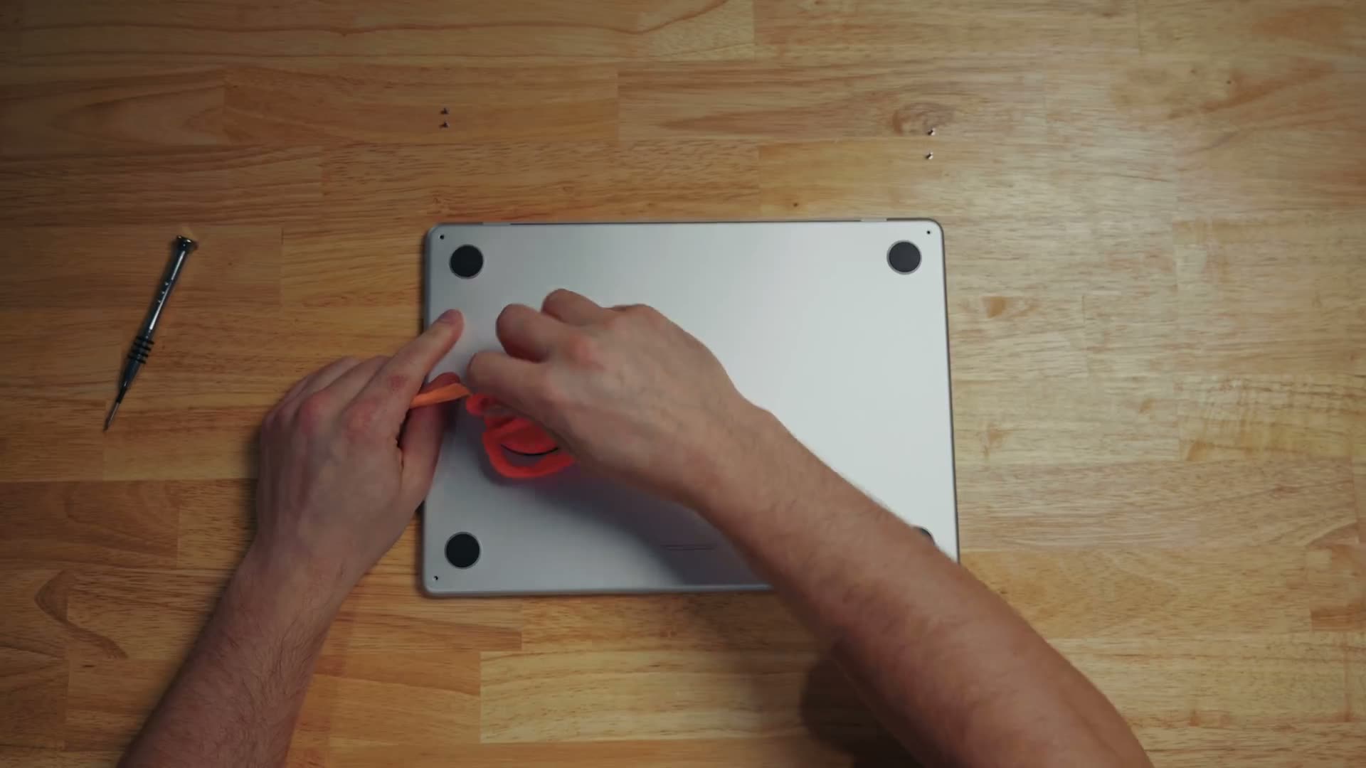 A suction cup on the bottom case of a MacBook Air while an orange plastic pry tool is worked into the seam