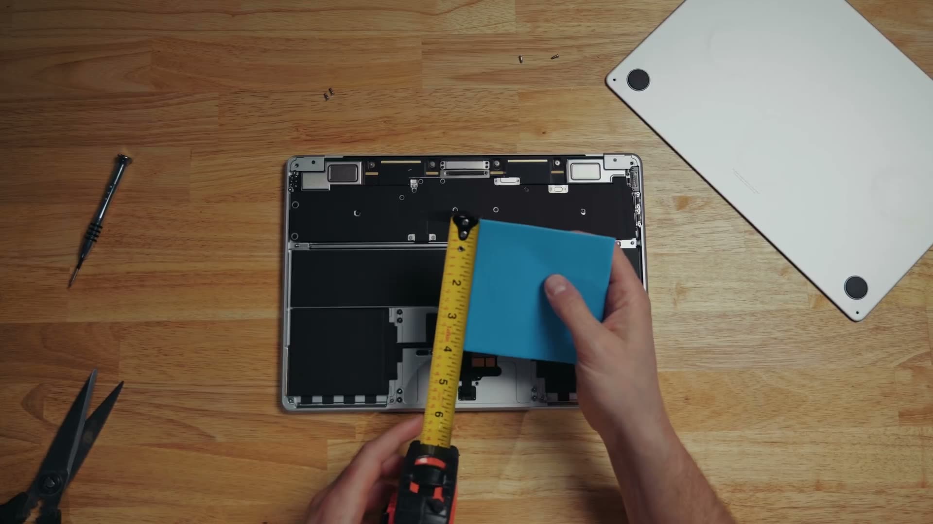A blue thermal pad measured against a tape measure over the opened interior of an M5 MacBook Air