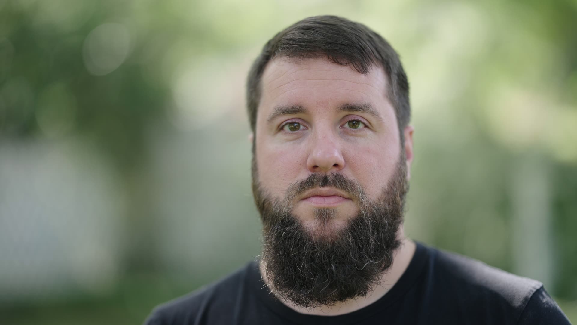 Medium close-up portrait filmed outdoors on the Sigma 85mm F1.2, with the subject separated from a soft green background