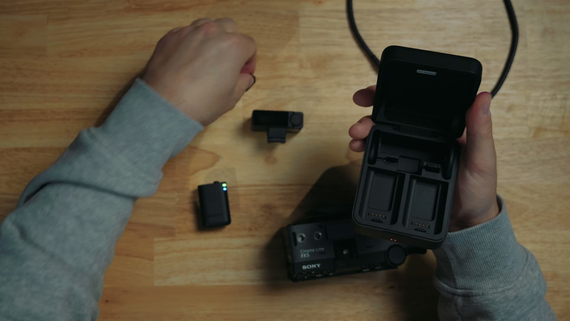Sony ECM-W5 charging case open on a wooden desk next to a transmitter, the receiver and a Sony FX5