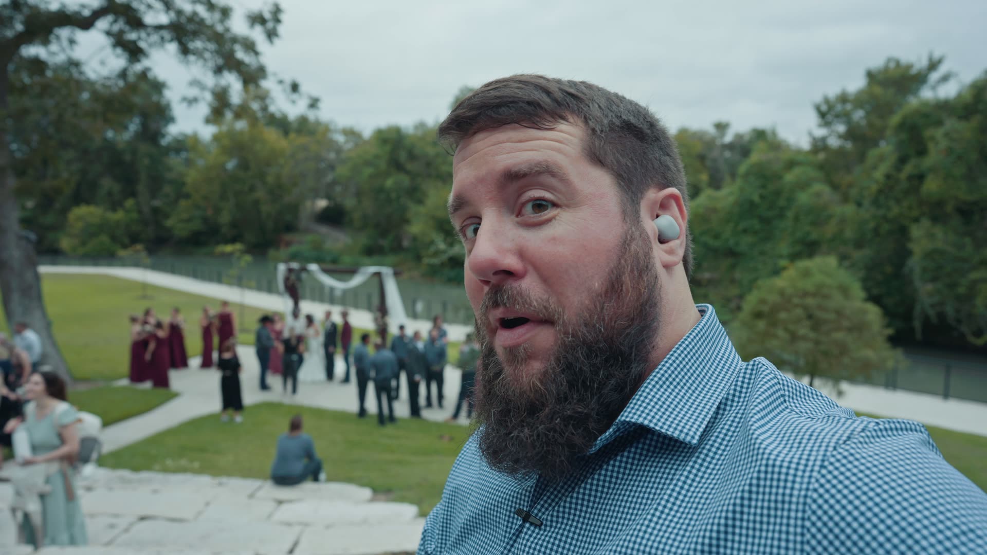Matt Johnson at an outdoor wedding ceremony pointing to a Sony earbud in his ear while monitoring audio